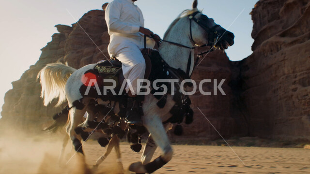 علاقة أبناء الوطن بالخيل الأصيل، توارث حب الجياد من الأجداد إلى الأبناء، التشكيلات والتكوينات الصخرية الطبيعية في صحراء السعودية، صورة مقربة لرجل عربي خليجي سعودي يمتطي الفرس، التجول في الطبيعة الصحراوية على ظهر الحصان
