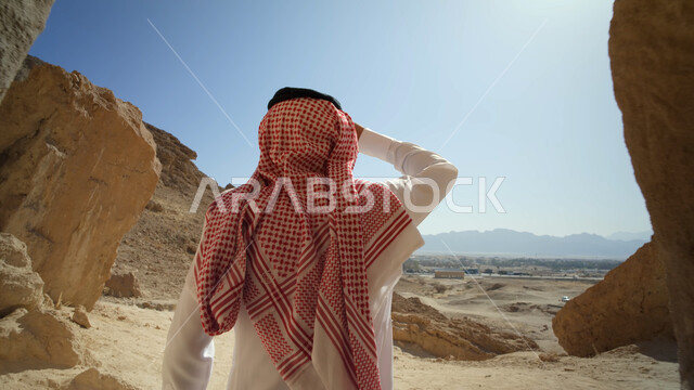 رحلات السفاري في الصحراء، التشكيلات والتكوينات الصخرية في السعودية، معالم وأماكن سياحية في المملكة، رجل عربي خليجي سعودي يرتدي الزي التقليدي يقف داخل كهف في المنطقة الصحراوية، الاستمتاع بالمناظر الطبيعية