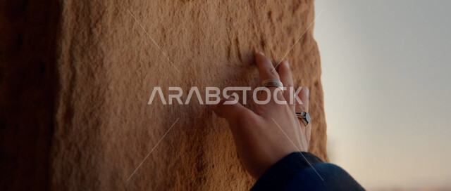 التشكيلات والتكوينات الصخرية، الاستمتاع بالمناظر الطبيعية، مناطق الرحلات وقضاء الوقت الممتع, أماكن ومعالم السياحة المشهورة, صورة مقربة ليد امرأة عربية خليجية سعودية تقوم بلمس الجدران الطينية