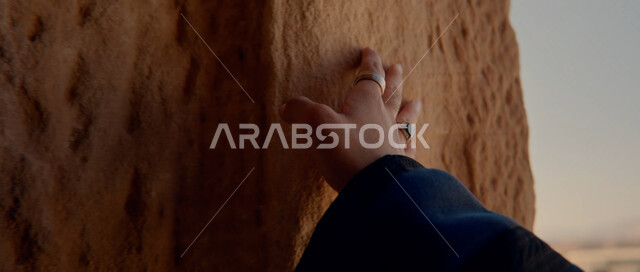 Rock formations and formations, enjoying the natural scenery, areas for excursions and spending a good time, famous tourist places and landmarks, a close-up photo of the hand of a Saudi Gulf Arab woman touching the clay walls
