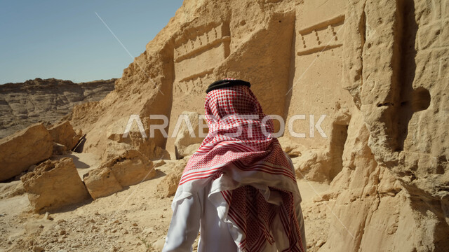 التكوينات والتشكيلات الصخرية، زيارة المناطق السياحية في صحراء المملكة العربية السعودية، صورة مقربة لرجل عربي خليجي سعودي يرتدي الزي التقليدي يقوم بالنظر إلى المعالم التاريخية