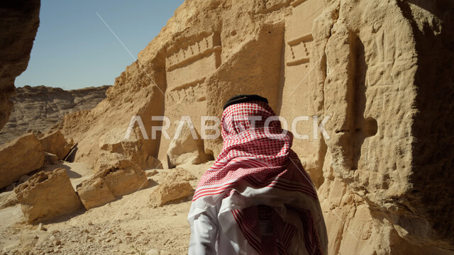 التشكيلات والتكوينات الصخرية، زيارة المناطق السياحية في صحراء المملكة العربية السعودية، صورة مقربة لرجل عربي خليجي سعودي يرتدي الزي التقليدي يقوم بالنظر إلى المعالم التاريخية