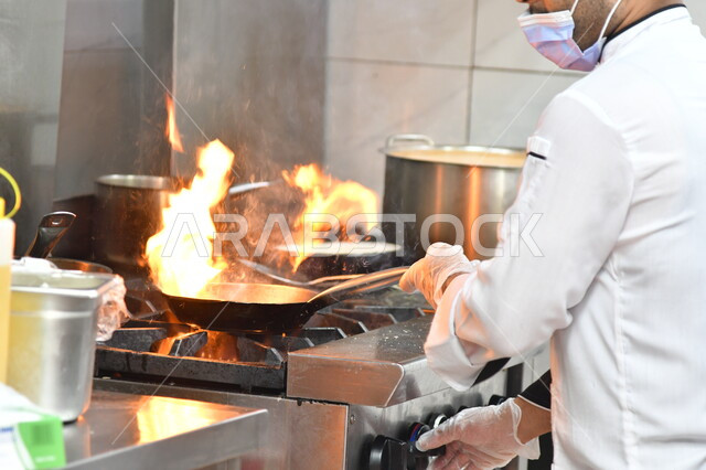 اعداد وتحضير الطعام في مطابخ و مطاعم المملكة العربية السعودية، صورة مقربة لشيف عربي خليجي سعودي يقوم بطهي الغداء في المقلاة على موقد الغاز، أطعمة ومأكولات شرقية لذيذة، وجبة ذات قيمة غذائية عالية