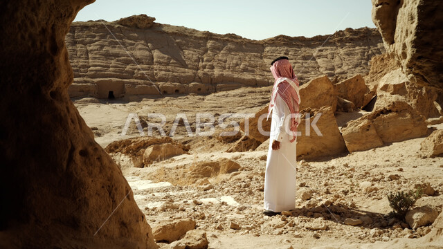 أماكن سياحية في المملكة، التكوينات والتشكيلات الصخرية الطبيعية في السعودية، صورة من الجانب لرجل عربي خليجي سعودي يرتدي الزي التقليدي يسير في الطرقات الصحراوية المتعرجة