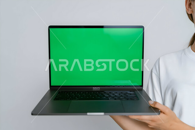 استخدام التكنولوجيا الحديثة والمتطورة للتعلم عن بعد، القيام بمقابلات وإجتماعات العمل أونلاين، صورة مقربة لأيدي رجل عربي خليجي سعودي يمسك بيده الحاسب المحمول بشاشة خضراء فارغة، متابعة أخبار وسائل التواصل الإجتماعي، كروما