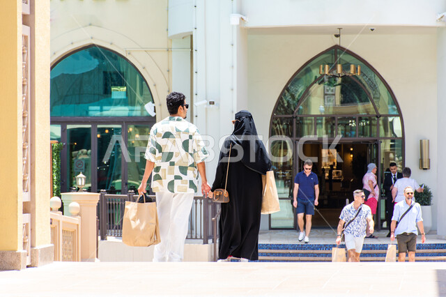 أنشطة ترفيهية مسلية مع العائلة, صورة من الخلف لزوجان عربيان خليجيان سعوديان يستعدون للتسوق في دبي مول, أماكن ومعالم سياحية مشورة في الامارات العربيه المتحدة, قضاء أوقات ممتعه مع الاسرة في العطلة الصيفية, الاستفادة من العروض والخصومات