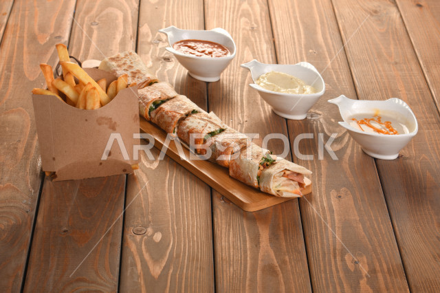 A plate of chicken sandwich in tortilla bread on a wooden table, a group of delicious sauces, delicious meals, fast food, Arabic restaurant