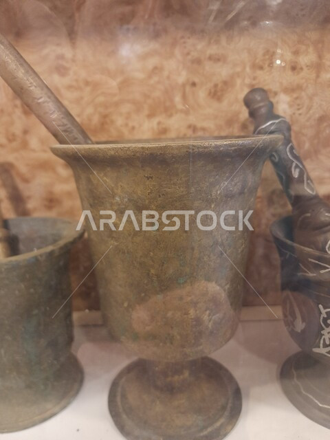 استخدام وعاء وعصا الهاون للطحن في المملكة, أدوات منزلية تقليدية شعبية تراثية, معالم السياحة المشهورة في السعودية, المهباش السعودي القديم, صورة مقربة  لمدقة الطحن النحاسي والخشبي في متحف قرية مطير العيش في محافظة الحجرة في منطقة الباحة