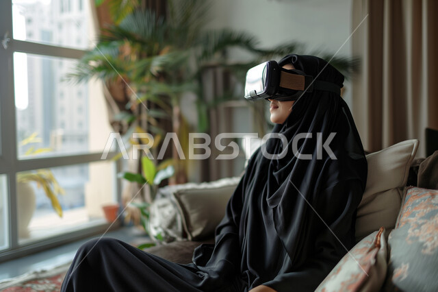 Interaction, integration, and simulation of the imaginary world, a close-up image of a veiled Saudi Arabian Gulf woman wearing virtual reality glasses sitting on a comfortable chair, the concept of entertainment and entertainment, spending a good time, the development of technology and technology