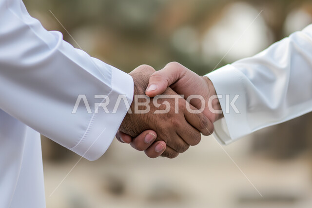 الشراكة في الأعمال والمشاريع، صداقات وتعارف وبناء علاقات اجتماعية، عقد صفقات عمل جديدة ناجحة، صورة مقربة لايدي رجلان عربيان خليجيان سعوديان يقومان بمصافحة بعضهما، توسيع مجالات العمل، خلفية ضبابية
