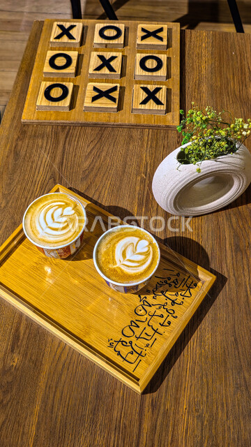 مشروب الكابتشينو الساخن ، صورة من الاعلى لكوب من القهوة برغوة كثيفة مع رسومات على قاعدة خشبية، مشروبات ساخنة لذيذة ،كافيهات ومطاعم سلطنة عمان