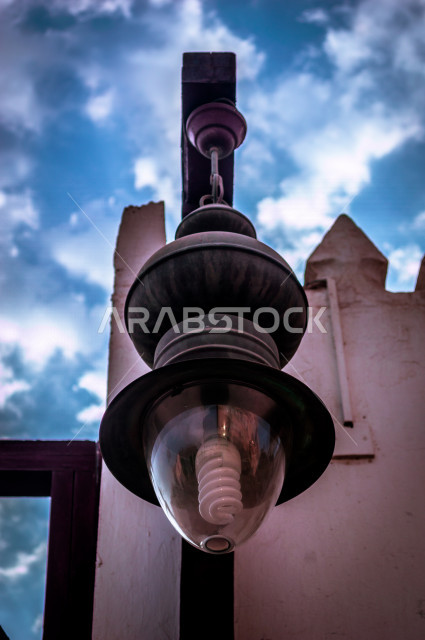 ضوء الشارع المعدني الأسود تحت السماء الزرقاء في المملكة العربية السعودية , منظر زاوية منخفضة للمصباح الكهربائي , ضوء الشارع معزول ضد خلفية السماء الزرقاء غائم في يوم صيف مشرق , عمود مصباح الشارع , الصورة المقربة , معالم تاريخية أثرية