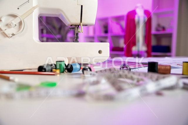 ورشة خياطة (مكان عمل) لتصميم الأزياء الإبداعي مع أدوات وماكينة خياطة وأقمشة وقوالب وخيوط بألوان مختلفة , مكتب مصمم حديث ملهم , أتيلييه خياطة مع عارضة أزياء (مانيكان) بقماش وردي ,  مكان عمل الخياطة , صالة واستديو التصميم