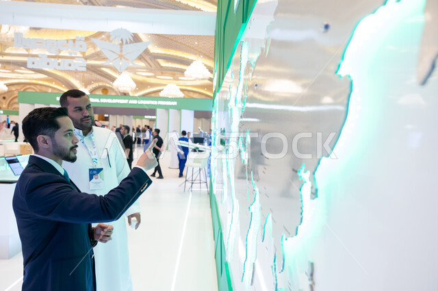 الوقوف امام شاشة الكترونيه ثلاثية الابعاد لخريطة العالم، رؤية مستقبلية سعودية 2030، حوارات ومناقشات عالميه، رجل عربي سعودي خليجي مع رجل يرتدي البدله الرسميه في مؤتمر مستقبل الطيران في مدينة الرياض، توسيع سبل التعاون في قطاع الطيران المدني