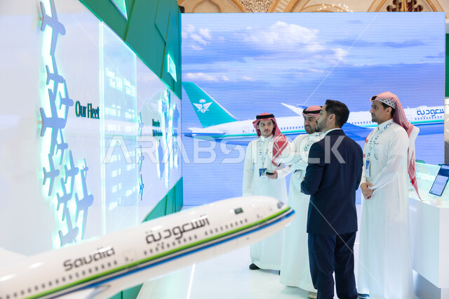 Global discussions and dialogues, Saudi Vision 2030, Saudi Arabian Gulf men with a man wearing a formal suit at the Future of Aviation Conference in Riyadh, standing in front of a 3D electronic screen of a world map, expanding cooperation in the civil aviation sector
