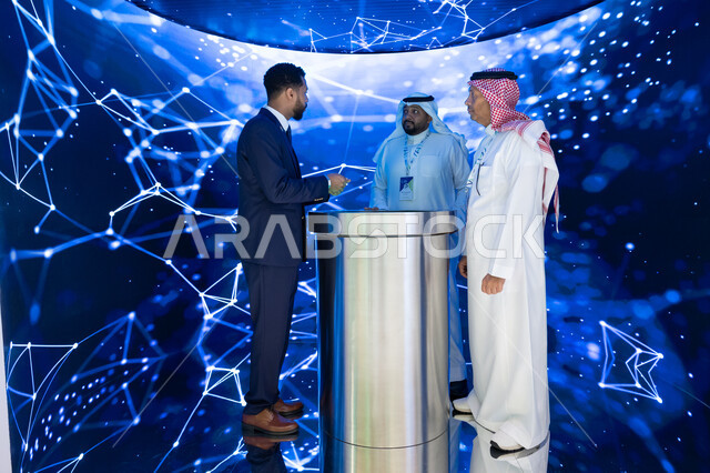 شاشة الكترونيه ثلاثية الابعاد لمخططات هولوجرامية، توسيع سبل التعاون في قطاع الطيران المدني، رؤية مستقبلية سعودية 2030، حوارات ومناقشات عالميه، رجلان عربيان سعوديان خليجيان مع رجل يرتدي البدله الرسميه يقفان في مؤتمر مستقبل الطيران في مدينة الرياض