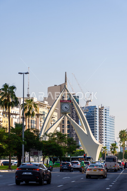 الفن الهندسي المعماري على الطراز الحديث لبرج الساعة في ديرة في مدينة دبي وقت النهار، التقدم والنمو العمراني في الإمارات العربية المتحدة، معالم وأماكن سياحية مشهورة، حركة المرور للسيارات في الطرقات والشوارع الاسفلتية، المباني والمنشآت السكنية والتجارية