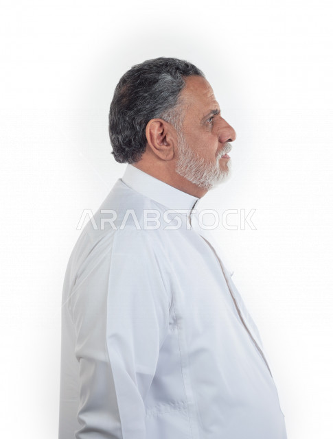 بورتريه رجل عربي سعودي كبير بالسن يقوم بجلسات التصوير , يرتدي ثوب أبيض , خلفية بيضاء , منظر جانبي لرجل مسن يلتقط الصور مفهوم تعبيرالوجه ولغة الجسد