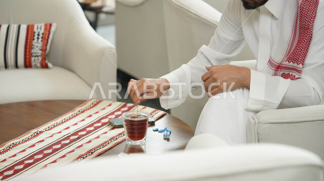 كرم الضيافة وحسن الاستقبال، العادات والتقاليد في المملكة العربية السعودية، صورة مقربة لرجل عربي خليجي سعودي يرتدي الثوب التقليدي يحمل بيده كوب زجاجي من الشاي، الاستمتاع بالمشروبات الساخنة في المجالس العربية