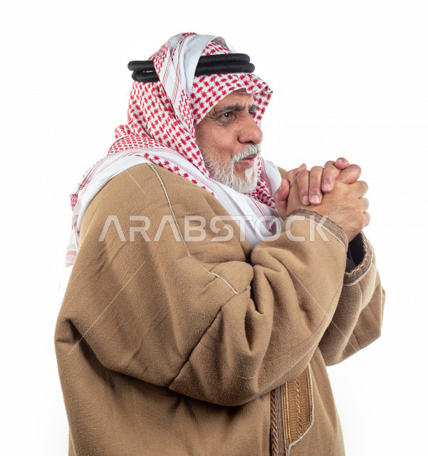 بورتريه رجل عربي سعودي كبير بالسن يشعر بالبرد , يرتدي البشت السعودي مع شماغ وعقال , خلفية بيضاء , منظر جانبي لرجل مسن يشعربحالة من البرد والصقيع مفهوم لغة الجسد وتعابيرالوجه المختلفة