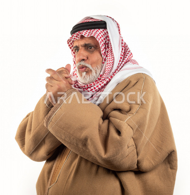 بورتريه رجل عربي سعودي كبير بالسن يشعر بالبرد , يرتدي البشت السعودي مع شماغ وعقال , خلفية بيضاء , رجل مسن يشعر بحالة من البرد والصقيع مفهوم لغة الجسد وتعابيرالوجه المختلفة