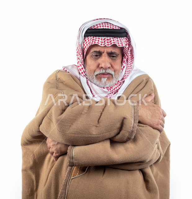 بورتريه رجل عربي سعودي كبير بالسن يشعر بالبرد , يرتدي البشت السعودي مع شماغ وعقال , خلفية بيضاء , رجل مسن يشعر بحالة من البرد والصقيع مفهوم لغة الجسد وتعابيرالوجه المختلفة