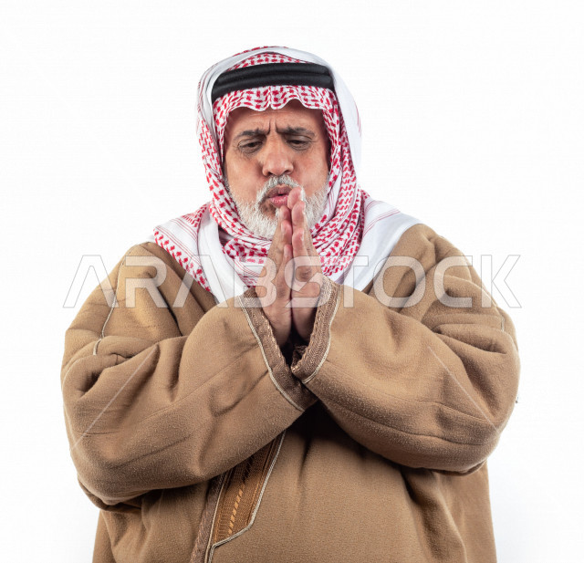 بورتريه رجل عربي سعودي كبير بالسن يشعر بالبرد , يرتدي البشت السعودي مع شماغ وعقال , خلفية بيضاء , رجل مسن يشعر بحالة من البرد والصقيع مفهوم لغة الجسد وتعابيرالوجه المختلفة