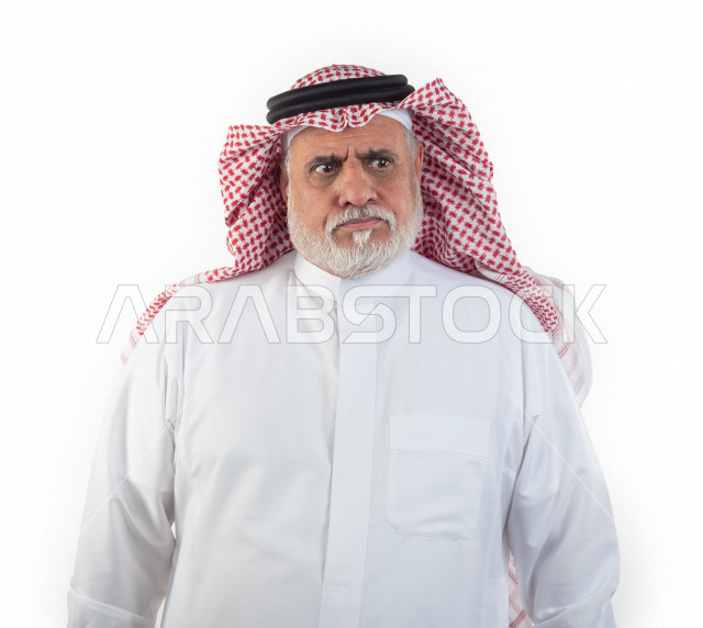 بورتريه رجل عربي سعودي كبير بالسن يقوم بجلسة تصوير في حالة من الغضب , صورة مقربة , شايب سعودي يرتدي ثوب أبيض مع شماغ وعقال , خلفية بيضاء , رجل مسن عبوس الوجه يلتقط الصور , مفهوم تعابيرالوجه