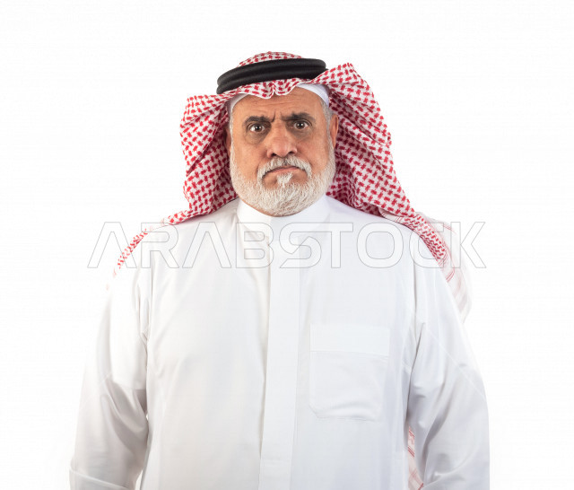 بورتريه رجل عربي سعودي كبير بالسن يقوم بجلسة تصوير في حالة من الغضب , صورة مقربة , شايب سعودي يرتدي ثوب أبيض مع شماغ وعقال , خلفية بيضاء , رجل مسن عبوس الوجه يلتقط الصور , مفهوم تعابيرالوجه