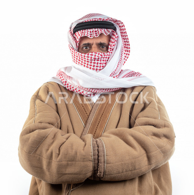 بورتريه رجل عربي سعودي كبير بالسن يشعر بالبرد , يرتدي البشت السعودي مع شماغ وعقال , خلفية بيضاء , رجل مسن يشعر بحالة من البرد والصقيع مفهوم لغة الجسد وتعابيرالوجه المختلفة