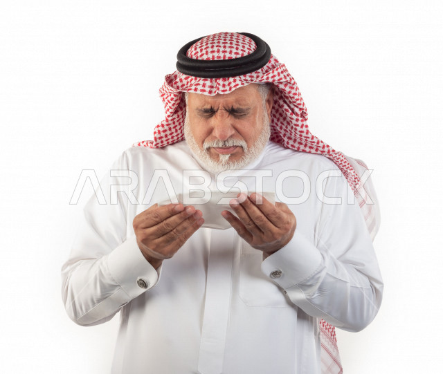 بورتريه رجل عربي سعودي كبير بالسن بيده منديل يضعه على أنفه والرغبة بالعطس , رجل شايب سعودي يرتدي ثوب أبيض مع شماغ وعقال , خلفية بيضاء , رجل مسن في حاله من العطس مفهوم لغة الجسد وتعابير الوجه