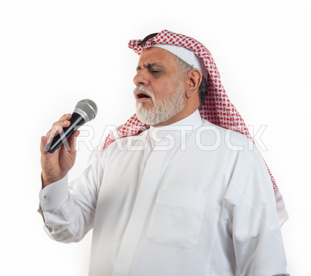 بورتريه رجل عربي سعودي كبير بالسن يحمل بيده ميكرفون في حالة من الاستمتاع , يرتدي ثوب أبيض مع شماغ وعقال , خلفية بيضاء , منظر جانبي لرجل مسن يستمتع بالغناء بالميكرفون مفهوم لغة الجسد وتعبيرالوجه 