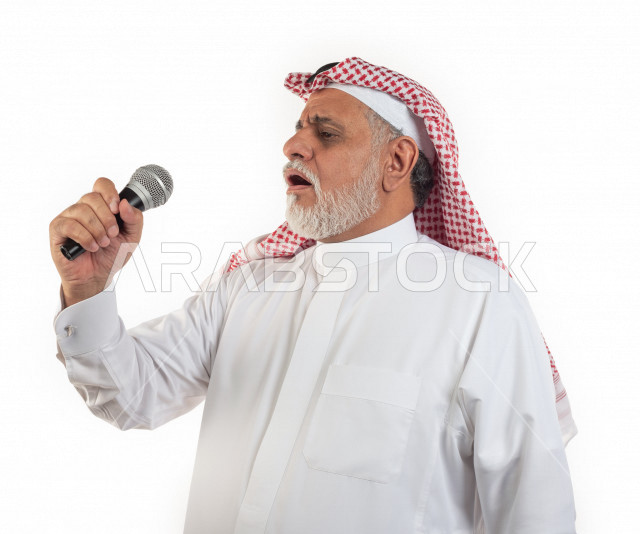 بورتريه رجل عربي سعودي كبير بالسن يحمل بيده ميكرفون في حالة من الاستمتاع , يرتدي ثوب أبيض مع شماغ وعقال , خلفية بيضاء , منظر جانبي لرجل مسن يستمتع بالغناء بالميكرفون مفهوم لغة الجسد وتعبيرالوجه 