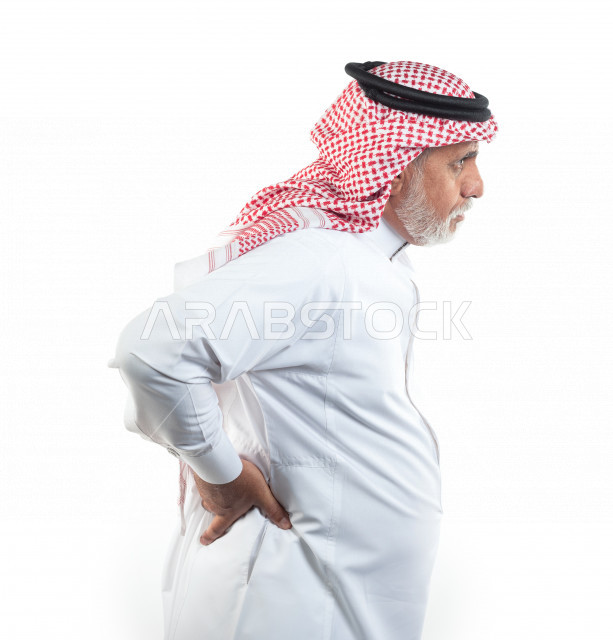 بورتريه رجل عربي سعودي كبير بالسن يضع يده على ظهره يشعر بحالة من الوجع والألم , صورة مقربة , شايب سعودي يرتدي ثوب أبيض مع شماغ وعقال , خلفية بيضاء , منظر جانبي لرجل مسن يشعر بالتعب والألم الشديد في ظهره , مفهوم تعابيرالوجه ولغة الجسد