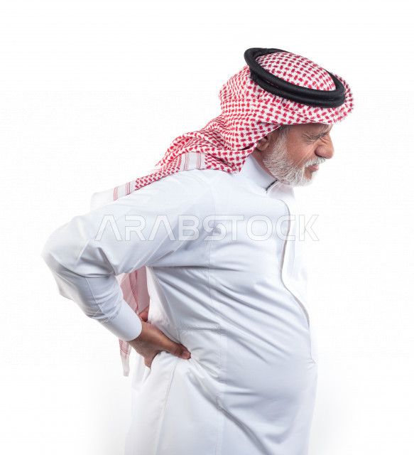 بورتريه رجل عربي سعودي كبير بالسن يضع يده على ظهره يشعر بحالة من الوجع والألم , صورة مقربة , شايب سعودي يرتدي ثوب أبيض مع شماغ وعقال , خلفية بيضاء , منظر جانبي لرجل مسن يشعر بالتعب والألم الشديد في ظهره , مفهوم تعابيرالوجه ولغة الجسد