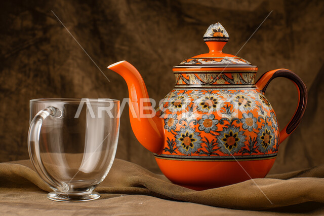 فنون تقديم المشروبات الساخنة، صورة مقربة لإبريق شاي مزخرف مع كوب من الشاي، الضيافة المتميزة في المملكة العربية السعودية، خلفية ملونة