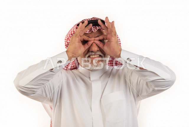 بورتريه رجل عربي سعودي كبير بالسن بإيماءات وجه ويدين مختلفة , صورة مقربة , شايب سعودي يرتدي ثوب أبيض مع شماغ وعقال , خلفية بيضاء , رجل مسن يلتقط الصور بتعابيرالوجه ولغة الجسد المختلفة