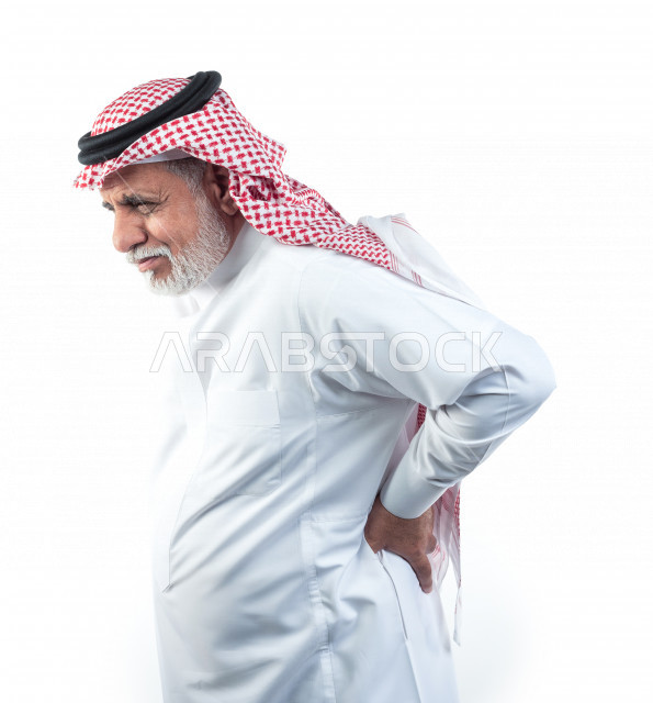 بورتريه رجل عربي سعودي كبير بالسن يضع يده على ظهره يشعر بحالة من الوجع والألم , صورة مقربة , شايب سعودي يرتدي ثوب أبيض مع شماغ وعقال , خلفية بيضاء , منظر جانبي لرجل مسن يشعر بالتعب والألم الشديد في ظهره , مفهوم تعابيرالوجه ولغة الجسد