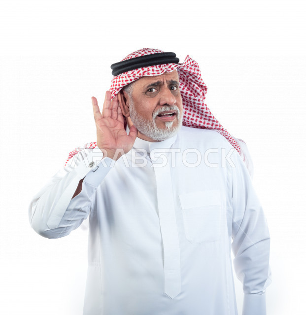 بورتريه رجل عربي سعودي كبير بالسن يضع يده على أذنه بإيماءات وجه ويدين مختلفة , صورة مقربة , شايب سعودي يرتدي ثوب أبيض مع شماغ وعقال , خلفية بيضاء , رجل مسن يلتقط الصور في حالة تنصت والإستماع بتعابيرالوجه ولغة الجسد المختلفة