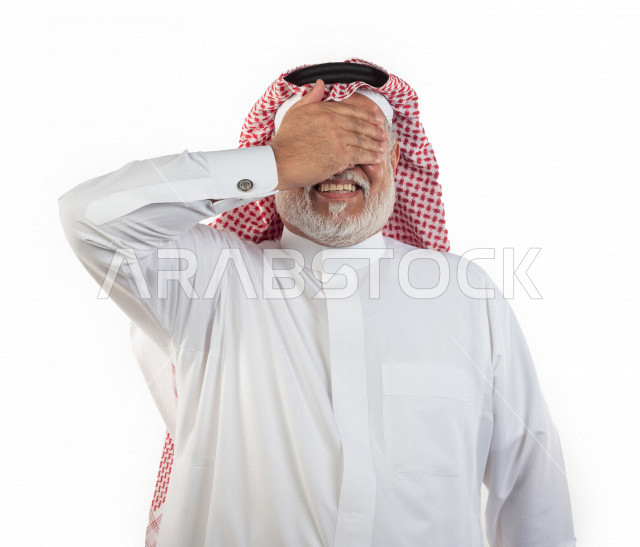 بورتريه رجل عربي سعودي كبير بالسن يضع يده على عينيه بإيماءات وجه ويدين مختلفة , صورة مقربة , شايب سعودي يرتدي ثوب أبيض مع شماغ وعقال , خلفية بيضاء , رجل مسن يلتقط الصور وهو مبتسم ويده على عينيه , مفهوم تعابيرالوجه ولغة الجسد المختلفة