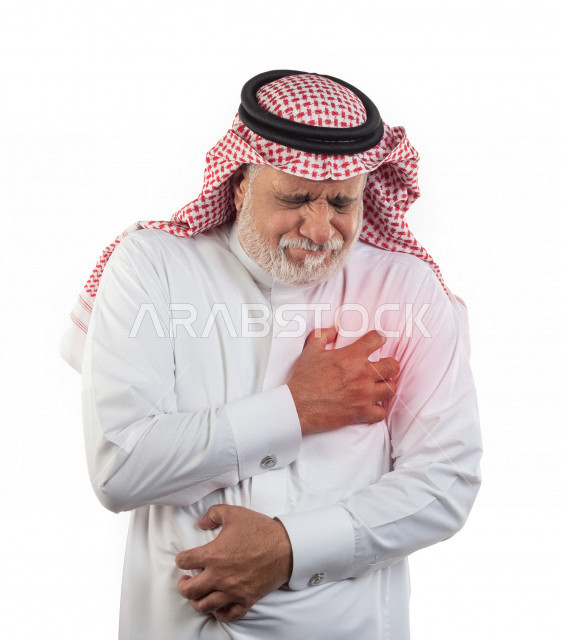 بورتريه رجل عربي سعودي كبير بالسن يضع يده على صدره يشعر بحالة من الوخز والألم بقلبه , صورة مقربة , شايب سعودي يرتدي ثوب أبيض مع شماغ وعقال , خلفية بيضاء , رجل مسن يشعر بالتعب والألم الشديد والوخز بصدره من جهه اليسار , مفهوم تعابيرالوجه ولغة الجسد