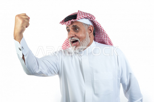بورتريه رجل عربي سعودي كبير بالسن يرفع قبضة يده وهو يبتسم بإيماءات وجه ويدين مختلفة , صورة مقربة , شايب سعودي يرتدي ثوب أبيض مع شماغ وعقال , خلفية بيضاء , رجل مسن يرفع يده في حالة من السعادة بالفوز والقوة , مفهوم تعابيرالوجه ولغة الجسد المختلفة