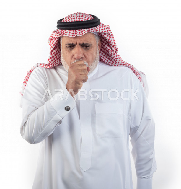 بورتريه رجل عربي سعودي كبير بالسن يضع يده أمام فمه وهو يسعل بإيماءات وجه ويدين مختلفة , صورة مقربة , شايب سعودي يرتدي ثوب أبيض مع شماغ وعقال , خلفية بيضاء , رجل مسن يسعل ويكح , مفهوم تعابيرالوجه ولغة الجسد المختلفة