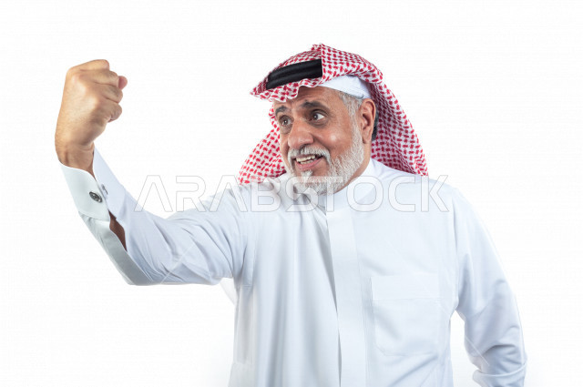 بورتريه رجل عربي سعودي كبير بالسن يرفع قبضة يده وهو يبتسم بإيماءات وجه ويدين مختلفة , صورة مقربة , شايب سعودي يرتدي ثوب أبيض مع شماغ وعقال , خلفية بيضاء , رجل مسن يرفع يده في حالة من السعادة بالفوز والقوة , مفهوم تعابيرالوجه ولغة الجسد المختلفة
