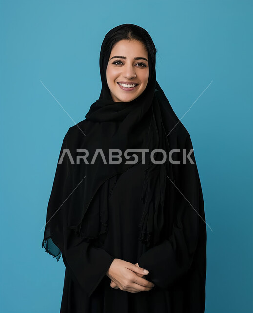 ايماءات السعادة والسرور، الصور الشخصية للوثائق الرسمية، الأزياء العصرية للمحجبات، الإهتمام بالمظهر الخارجي والأناقة، مفهوم الأنوثة والنعومة، بورتريه لامرأة عربية خليجية سعودية محجبة ترتدي عباءة سوداء تنظر الى الكاميرا وتقف باستقامة، خلفية زرقاء