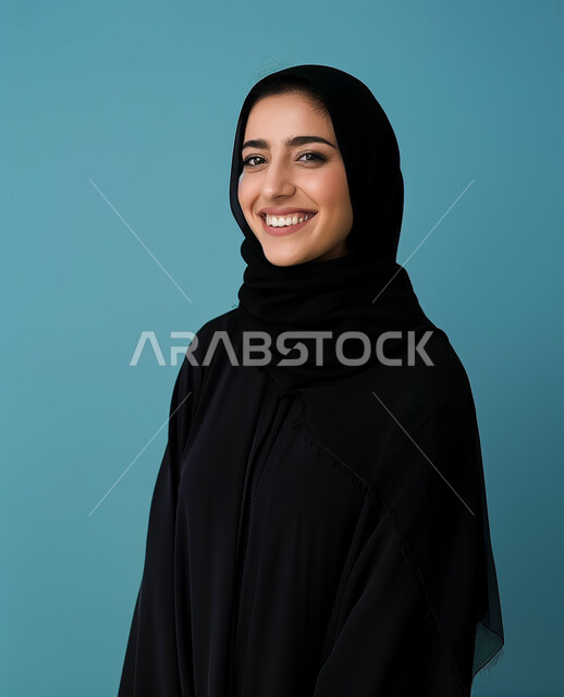 الملابس العصرية للمحجبات، الإهتمام بالمظهر الخارجي والأناقة، مفهوم الأنوثة والنعومة، بورتريه مقرب لامرأة عربية خليجية سعودية محجبة ترتدي عباءة سوداء تنظر الى الكاميرا بايماءات السعادة والسرور، التقاط الصور الشخصية للوثائق الرسمية، خلفية زرقاء