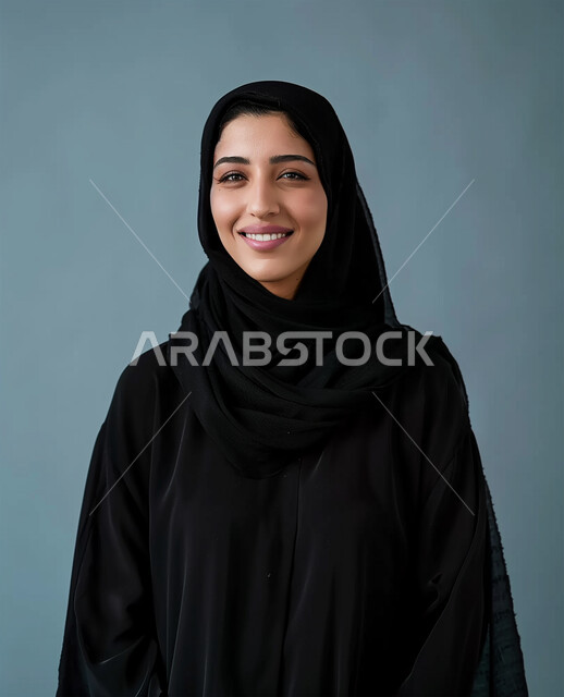الملابس العصرية للمحجبات، الأناقة والإهتمام بالمظهر الخارجي، مفهوم النعومة والأنوثة، ايماءات السعادة والسرور، الصور الشخصية للوثائق الرسمية، بورتريه مقرب لامرأة عربية خليجية سعودية محجبة ترتدي عباءة سوداء تنظر الى الكاميرا وتقف باستقامة، خلفية رمادية