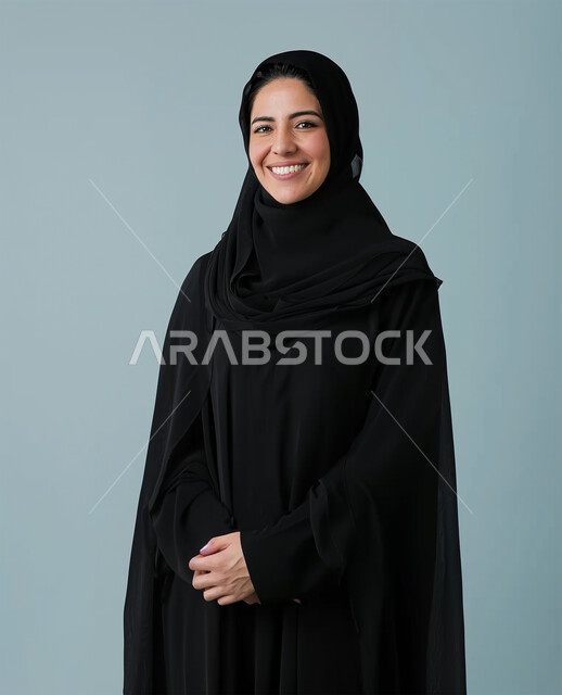 Softness, femininity, interest in appearance and elegance, gestures of happiness and pleasure, personal photos for official documents, modern fashion for veiled women, close-up portrait of a veiled Saudi Arabian Gulf woman wearing a black abaya looking at the camera and standing straight, gray background