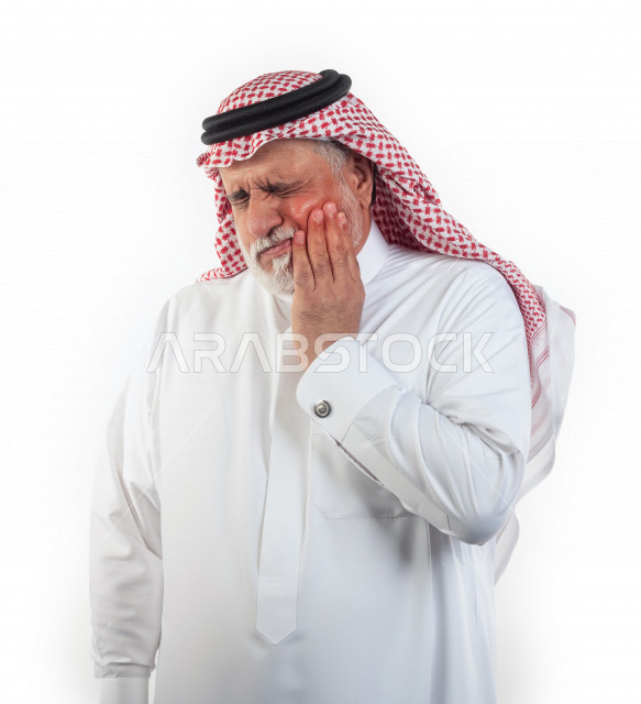 Portrait of an old Saudi Arab man who puts his hand on his cheek and feels a state of pain and pain in the teeth, close-up, a young Saudi man wearing a white dress with a shemagh and headband, white background, an old man feeling tired and severe pain wit