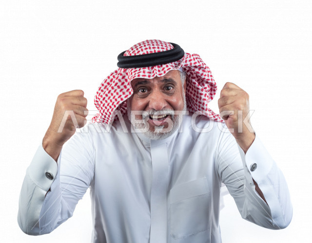 Portrait of an elderly Saudi Arab man raising his hands folded palms encouraging victory and victory, close-up, a young Saudi man wearing a white dress with a shemagh and headband, white background, an elderly man raising his hands while happy, the concep